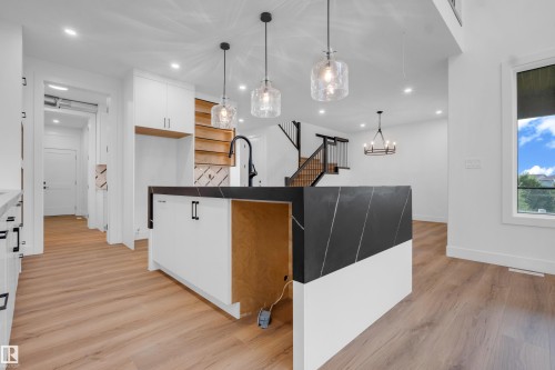 Kitchen island featuring a black and white waterfall countertop with veining, three clear glass pendant lights, a black gooseneck faucet, white cabinetry with black hardware, and wood-finish flooring - 57 Meadowgrove Lane, Spruce Grove, AB - Indoor Photo Showing Kitchen