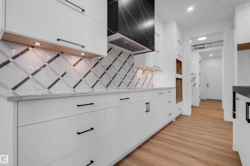 Contemporary kitchen featuring white cabinetry with matte black hardware, stone countertops, and a patterned tile backsplash - 57 Meadowgrove Lane, Spruce Grove, AB - Indoor Photo Showing Other Room