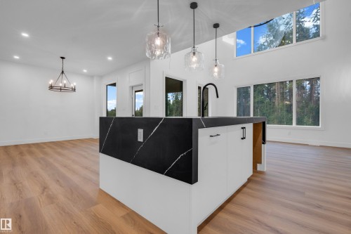 Modern kitchen island featuring a waterfall-edge countertop with white veining, integrated sink with a matte black faucet, and clear pendant lighting - 57 Meadowgrove Lane, Spruce Grove, AB - Indoor