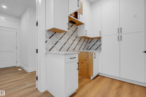 Compact kitchen area featuring white cabinetry with matte black hardware, a patterned tile backsplash, and light wood-finish flooring - 57 Meadowgrove Lane, Spruce Grove, AB - Indoor Photo Showing Other Room