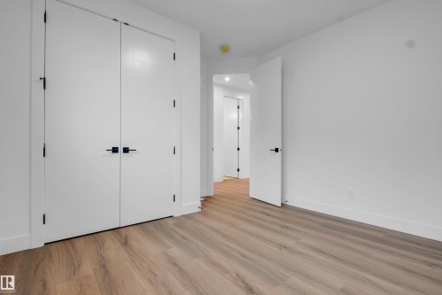 Spacious interior featuring wood-finish flooring, crisp white walls, and contemporary black hardware on doors - 57 Meadowgrove Lane, Spruce Grove, AB - Indoor Photo Showing Other Room