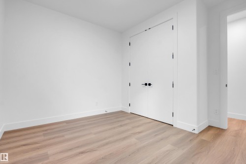 Crisp white walls frame a room featuring wood-finish flooring and a double-door closet with matte black hardware - 57 Meadowgrove Lane, Spruce Grove, AB - Indoor Photo Showing Other Room