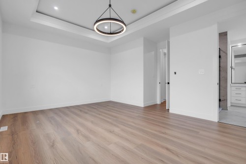 Spacious room featuring wood-finish flooring, a contemporary circular pendant light, and a tray ceiling with recessed lighting - 57 Meadowgrove Lane, Spruce Grove, AB - Indoor Photo Showing Other Room