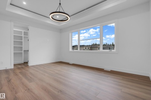 Spacious room featuring wood-finish flooring, a contemporary black circular chandelier, and a tray ceiling with recessed lighting - 57 Meadowgrove Lane, Spruce Grove, AB - Indoor Photo Showing Other Room