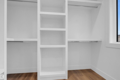Custom closet system featuring white built-in shelving, chrome hanging rods, and wood-finish flooring - 57 Meadowgrove Lane, Spruce Grove, AB - Indoor With Storage