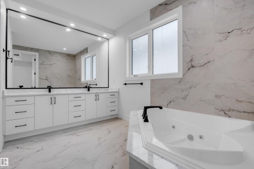 Contemporary bathroom featuring a white soaking tub with integrated jets, dual-sink vanity with white cabinetry, a large frameless mirror, and marble-look wall and floor tiling - 57 Meadowgrove Lane, Spruce Grove, AB - Indoor Photo Showing Bathroom