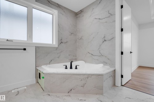 Corner jetted tub featuring matte black fixtures, surrounded by large format marble-look tile walls and flooring - 57 Meadowgrove Lane, Spruce Grove, AB - Indoor Photo Showing Bathroom