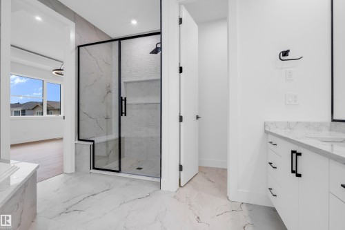 Spacious bathroom featuring a frameless glass shower enclosure with matte black accents, marble-look tile flooring, and a contemporary vanity with a stone countertop - 57 Meadowgrove Lane, Spruce Grove, AB - Indoor Photo Showing Bathroom