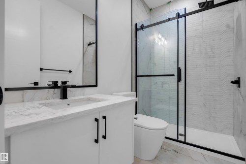 Modern bathroom featuring a white vanity with an integrated sink and light-toned countertop, black framed mirror, black matte fixtures, and a glass-enclosed shower with textured tile - 57 Meadowgrove Lane, Spruce Grove, AB - Indoor Photo Showing Bathroom