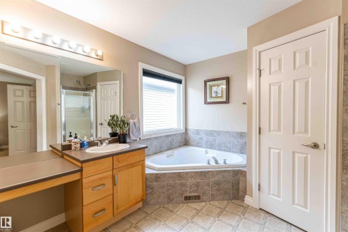Single vanity with wood cabinetry, integrated sink, and an expansive mirror - 5092 Thibault Way Nw, Edmonton, AB 