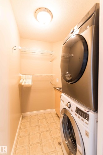 Stacked front-load washer and dryer, wire shelving, light wood-finish cabinetry, and patterned floor tile - 5092 Thibault Way Nw, Edmonton, AB 