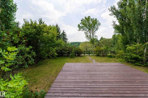 Expansive yard featuring a wood-finish deck, manicured lawn, lush trees, and a distant metal gate - 5092 Thibault Way Nw, Edmonton, AB 
