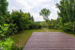 Expansive yard featuring a wood-finish deck, manicured lawn, lush trees, and a distant metal gate - 