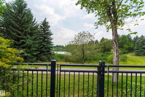 Black metal fencing bordering a paved path, a body of water, and mature trees - 5092 Thibault Way Nw, Edmonton, AB 