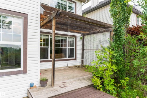 Expansive wood-finish deck with a pergola, white lattice privacy screen, and surrounding mature greenery - 5092 Thibault Way Nw, Edmonton, AB 