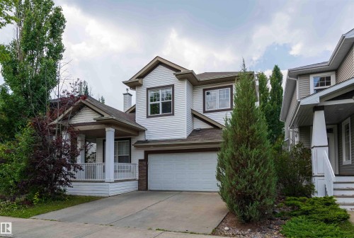 Two-story colonial featuring a light-colored vinyl exterior with peaked roofline and arched entry portico - 5092 Thibault Way Nw, Edmonton, AB 