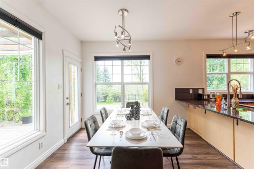 Spacious dining area featuring wood-finish flooring, multiple large windows, and a glass-paneled exterior door - 5092 Thibault Way Nw, Edmonton, AB 