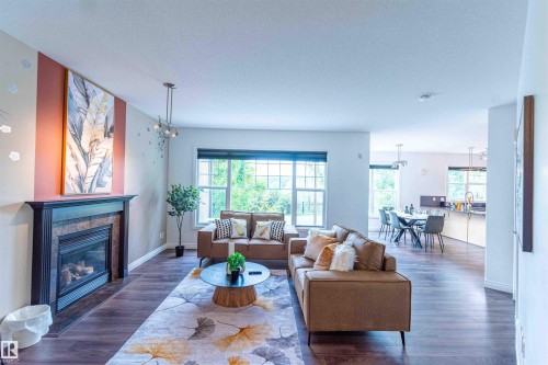 Open concept living space featuring wood-finish flooring, a built-in fireplace with a stone surround, and multiple windows - 5092 Thibault Way Nw, Edmonton, AB 