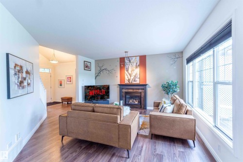 Living area featuring wood-finish flooring, a fireplace with a dark mantel, and large windows - 5092 Thibault Way Nw, Edmonton, AB 