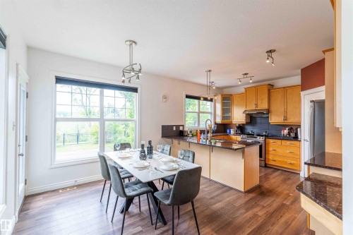 Wood-finish flooring, ample natural light from large windows, kitchen island with granite countertop, light wood cabinetry, and stainless steel appliances - 5092 Thibault Way Nw, Edmonton, AB 