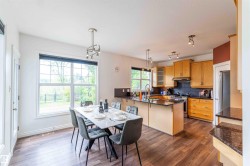 Wood-finish flooring, ample natural light from large windows, kitchen island with granite countertop, light wood cabinetry, and stainless steel appliances - 