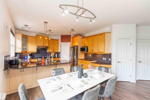 Open-concept kitchen and dining area featuring wood-finish flooring, light wood cabinetry, stone countertops, and a track lighting system - 5092 Thibault Way Nw, Edmonton, AB 