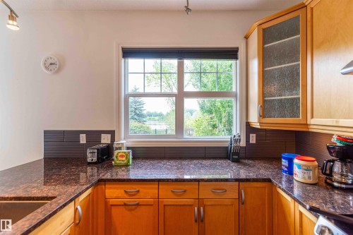 Kitchen featuring wood cabinetry, dark countertops, a window with a roller shade, and a tiled backsplash - 5092 Thibault Way Nw, Edmonton, AB 