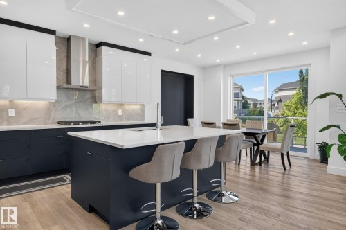 Contemporary kitchen featuring a large center island with seating, a built-in cooktop, and a stainless steel range hood - 16304 19 Avenue Sw, Edmonton, AB 