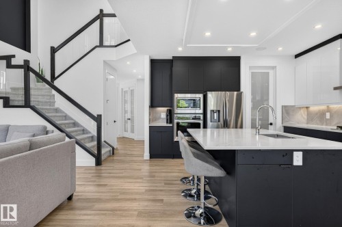 Open-concept kitchen featuring a large island with white stone-finish countertop, dark cabinetry, and stainless steel appliances - 16304 19 Avenue Sw, Edmonton, AB 