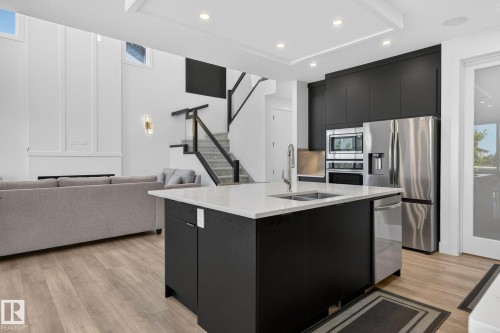 Modern kitchen featuring a central island with an undermount sink, white countertop, and dark cabinetry - 16304 19 Avenue Sw, Edmonton, AB 