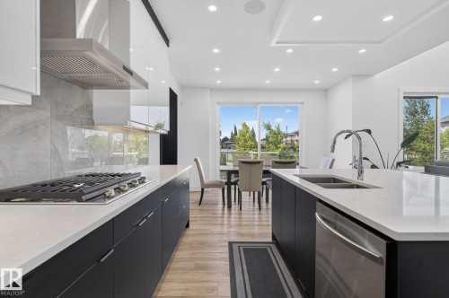 Contemporary kitchen featuring a gas range, stainless steel range hood, quartz countertops, dark lower cabinetry, and light upper cabinetry - 16304 19 Avenue Sw, Edmonton, AB 