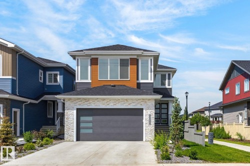 Contemporary two-story residence featuring a dark gray garage door with horizontal frosted glass inserts, a stone veneer facade, and a concrete driveway - 16304 19 Avenue Sw, Edmonton, AB 
