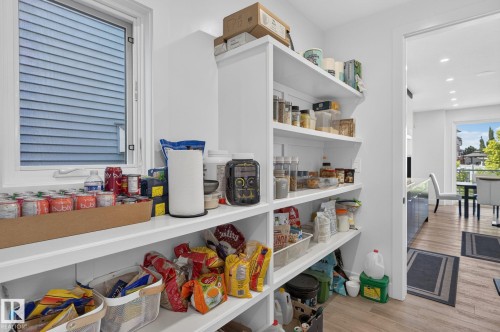 Expansive walk-in pantry featuring built-in shelving, a large window, and wood-finish flooring - 16304 19 Avenue Sw, Edmonton, AB 