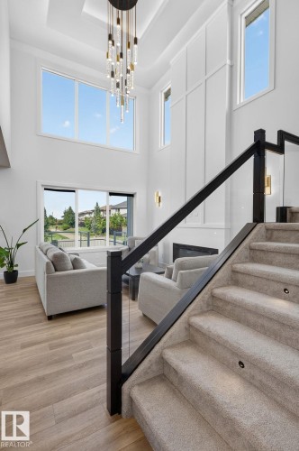 Staircase featuring carpeted treads with integrated lighting, glass balustrade, and dark wood-finish newel posts - 16304 19 Avenue Sw, Edmonton, AB 