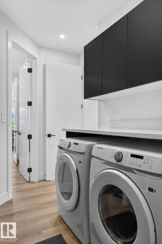 Laundry area featuring wood-finish flooring, a light gray countertop, and dark cabinetry - 16304 19 Avenue Sw, Edmonton, AB 