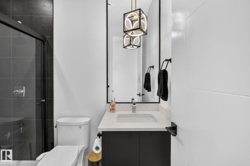 Contemporary bathroom featuring a dark tile shower with a frameless glass enclosure, a white toilet, and a vanity with a white countertop and dark cabinetry - 16304 19 Avenue Sw, Edmonton, AB 