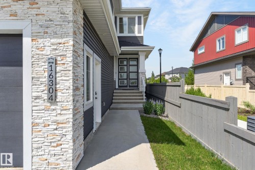 Modern exterior featuring stacked stone accents, horizontal siding, a contemporary entry door with frosted glass panels, concrete steps, and an integrated garage door - 16304 19 Avenue Sw, Edmonton, AB 