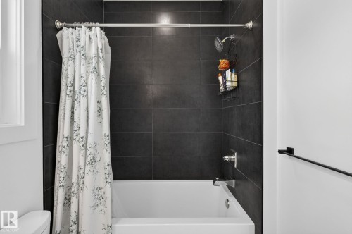 Tub and shower combination featuring dark tiled walls, a polished chrome shower head, and coordinating fixtures - 16304 19 Avenue Sw, Edmonton, AB 