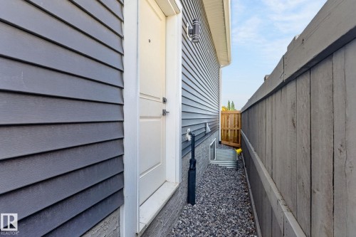Charcoal horizontal siding featuring a white trim door, gravel ground cover, and a wood privacy fence - 16304 19 Avenue Sw, Edmonton, AB 