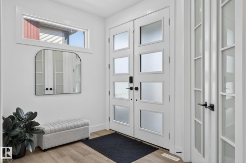 Entrance foyer with wood-finish flooring, featuring a transom window above the double entry doors - 16304 19 Avenue Sw, Edmonton, AB 