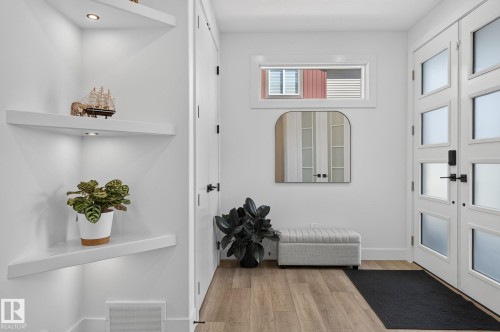 Entryway featuring wood-finish flooring, a contemporary front door with frosted glass panels, and a transom window - 16304 19 Avenue Sw, Edmonton, AB 