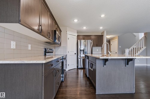 Kitchen featuring wood-finish flooring, recessed lighting, stone countertops, and stainless steel appliances - 1420 158 Street Sw, Edmonton, AB 