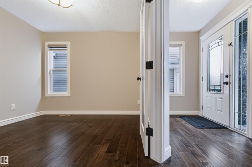 Dark wood-finish flooring throughout, light neutral wall paint, white trim, and a decorative glass panel entry door - 1420 158 Street Sw, Edmonton, AB 