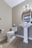 Pedestal sink with a circular mirror, wall-mounted vanity light, white toilet, and tile flooring - 