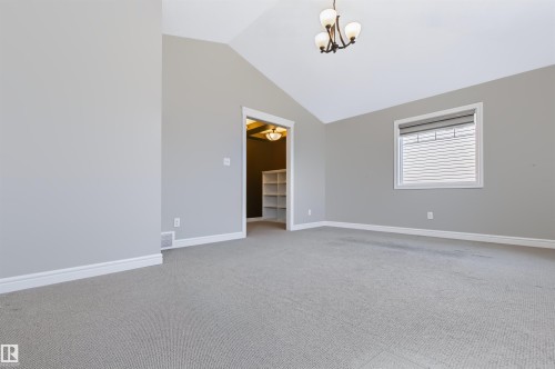 Vaulted ceiling featuring a decorative chandelier, neutral wall paint, light-colored carpet, and a window with blinds - 1420 158 Street Sw, Edmonton, AB 