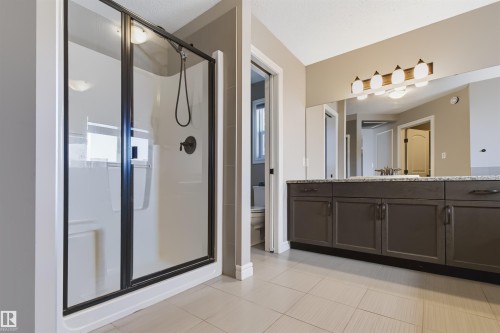 Black-framed glass shower enclosure with a built-in shower bench, an extended vanity with dual sinks, a large mirror, and ceramic tile flooring - 1420 158 Street Sw, Edmonton, AB 