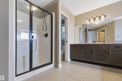 Black-framed glass shower enclosure with a built-in shower bench, an extended vanity with dual sinks, a large mirror, and ceramic tile flooring - 