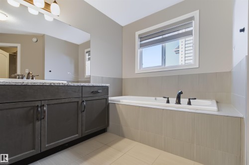 Built-in soaker tub with dark bronze fixtures, tile surround, and an integrated window - 1420 158 Street Sw, Edmonton, AB 