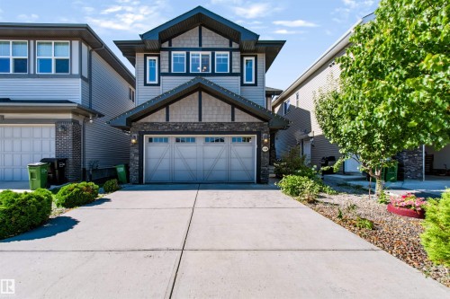 Contemporary exterior featuring a stone and siding facade, a double-car garage, an extended concrete driveway, decorative exterior lighting, and mature landscaping - 1420 158 Street Sw, Edmonton, AB 