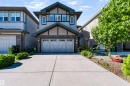 Contemporary exterior featuring a stone and siding facade, a double-car garage, an extended concrete driveway, decorative exterior lighting, and mature landscaping - 1420 158 Street Sw, Edmonton, AB 